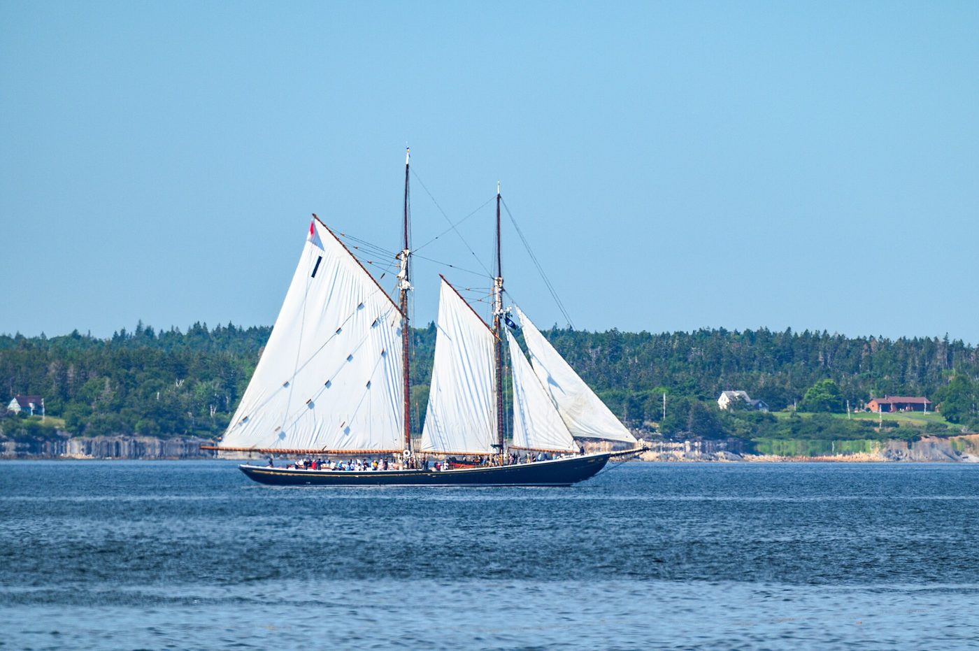 Bluenose II under sail off Blue Rocks near Lunenburg in 2022, black hull, white sails, a small crowd of people on deck.