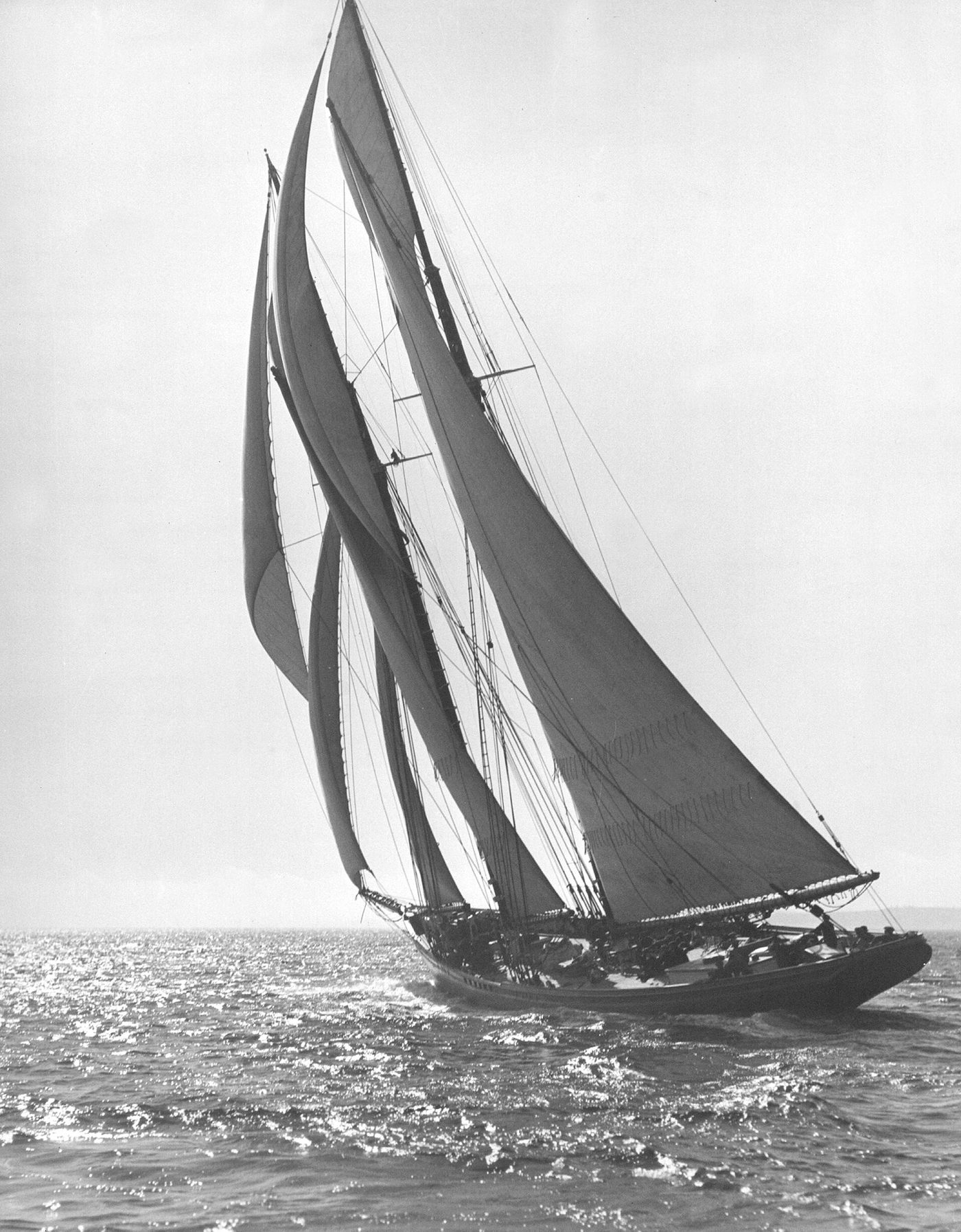 The Bluenose heeled hard under full sail, crew on deck, photographed from astern as she sails away, 1921.
