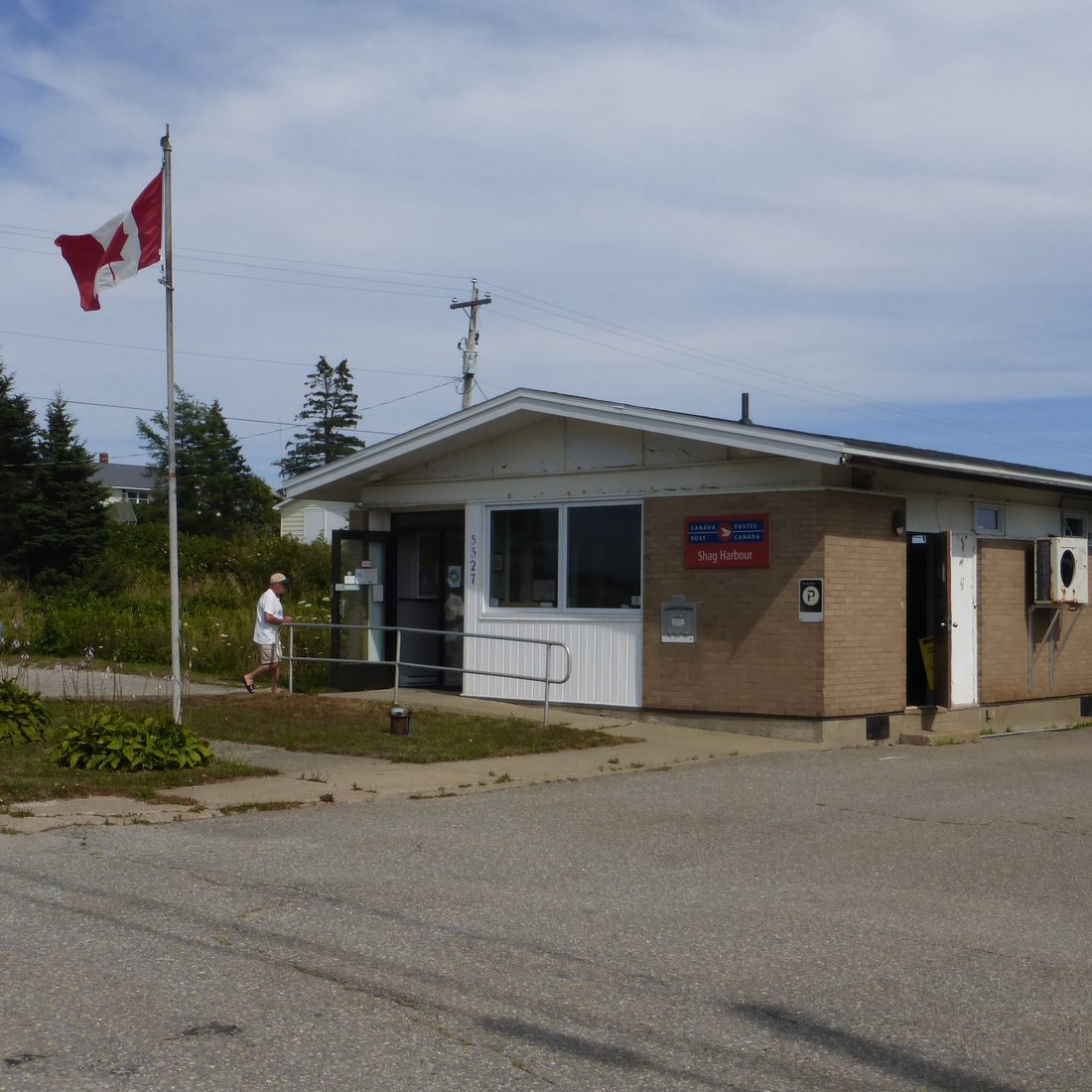 A small one-storey post office with a Canadian flag on a pole beside the road.